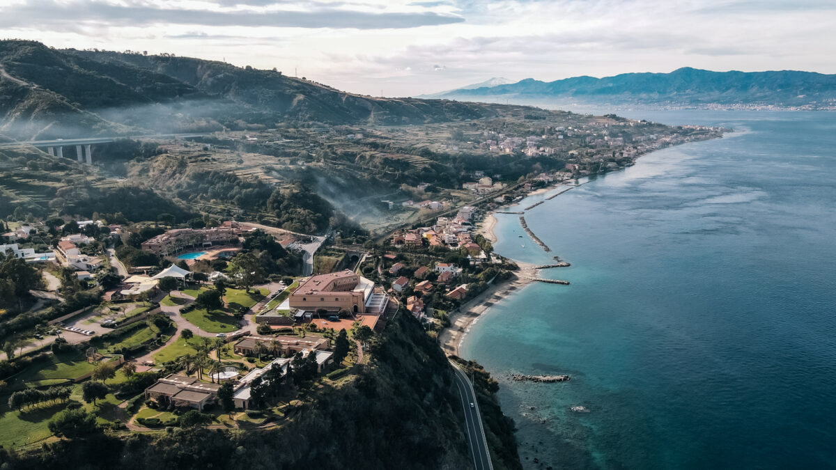 Immagine aerea di Altafiumara Resort & Spa che cattura la sua architettura unica e la posizione pittoresca lungo la Costa Viola, con il mare cristallino e le colline verdi circostanti.